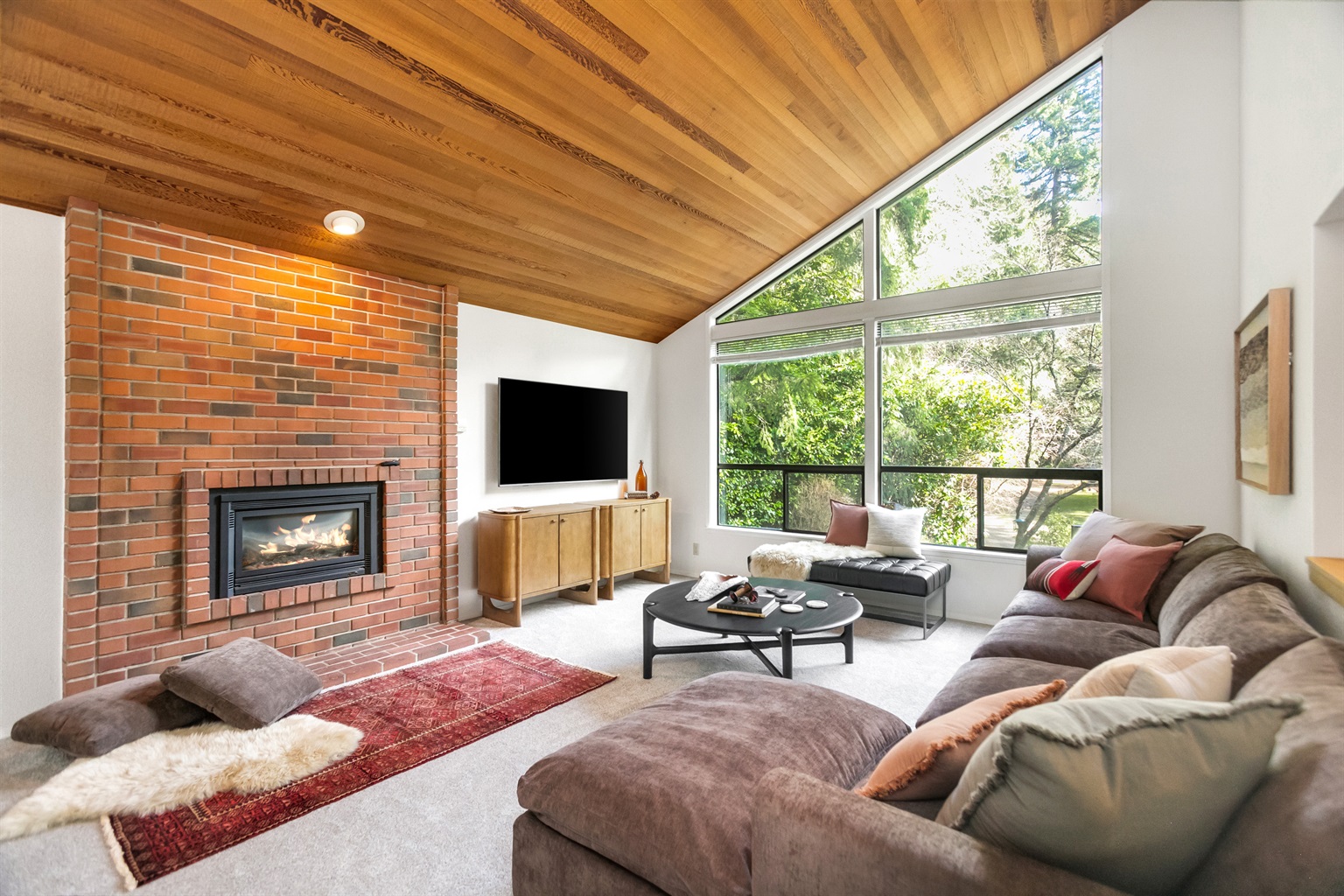 Spacious and vaulted living room features valued cedar ceilings, a gas fireplace, cloud couch, and a 65-inch television.