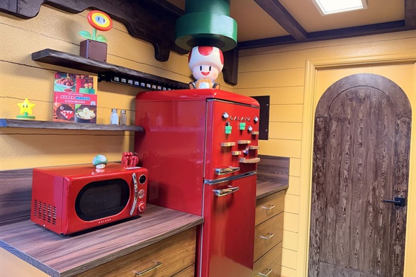 Full Mario kitchen corner featuring the bright red retro fridge and microwave at Mario's Mini Mansion, Clermont, FL. Toad figurine on top and fun shelves complete this vibrant, family-friendly cooking space. Wooden door leads to a Yoshi's Fort room!