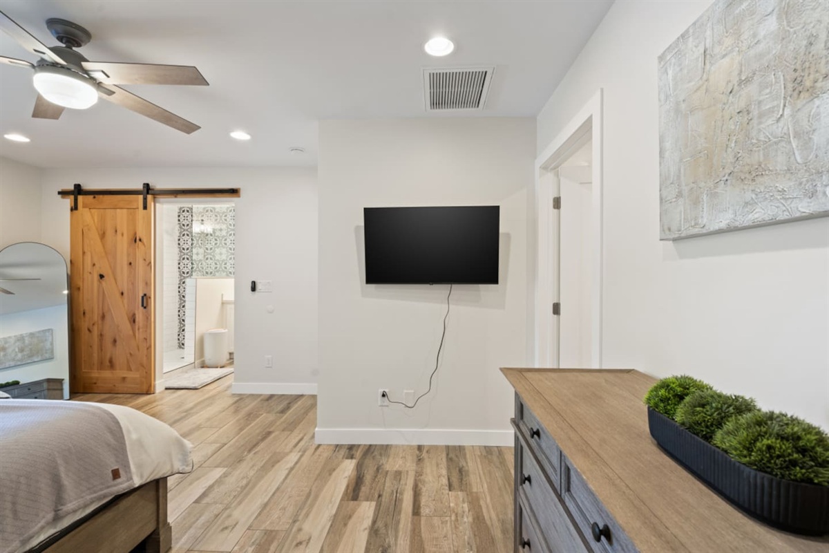 Main ensuite bedroom with queen bed, clean bedding, storage, tv, and a simple restful layout.