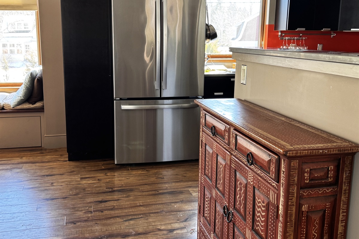 Bright kitchen entrance on the main level featuring a stainless steel refrigerator and modern cabinetry. A sun-filled built-in window seat offers a cozy nook to read or watch life in the historic village of Otter Creek.