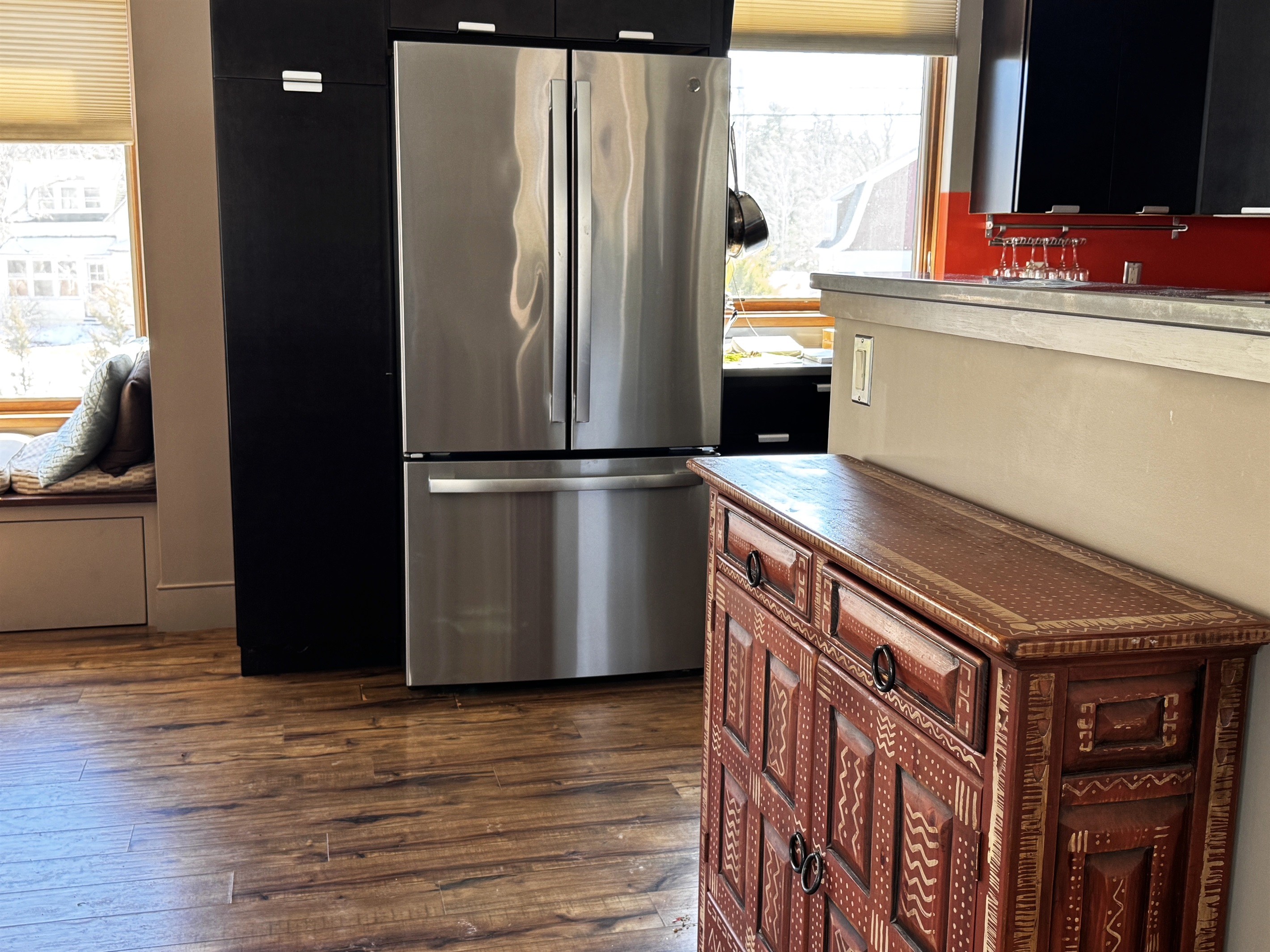 Bright kitchen entrance on the main level featuring a stainless steel refrigerator and modern cabinetry. A sun-filled built-in window seat offers a cozy nook to read or watch life in the historic village of Otter Creek.