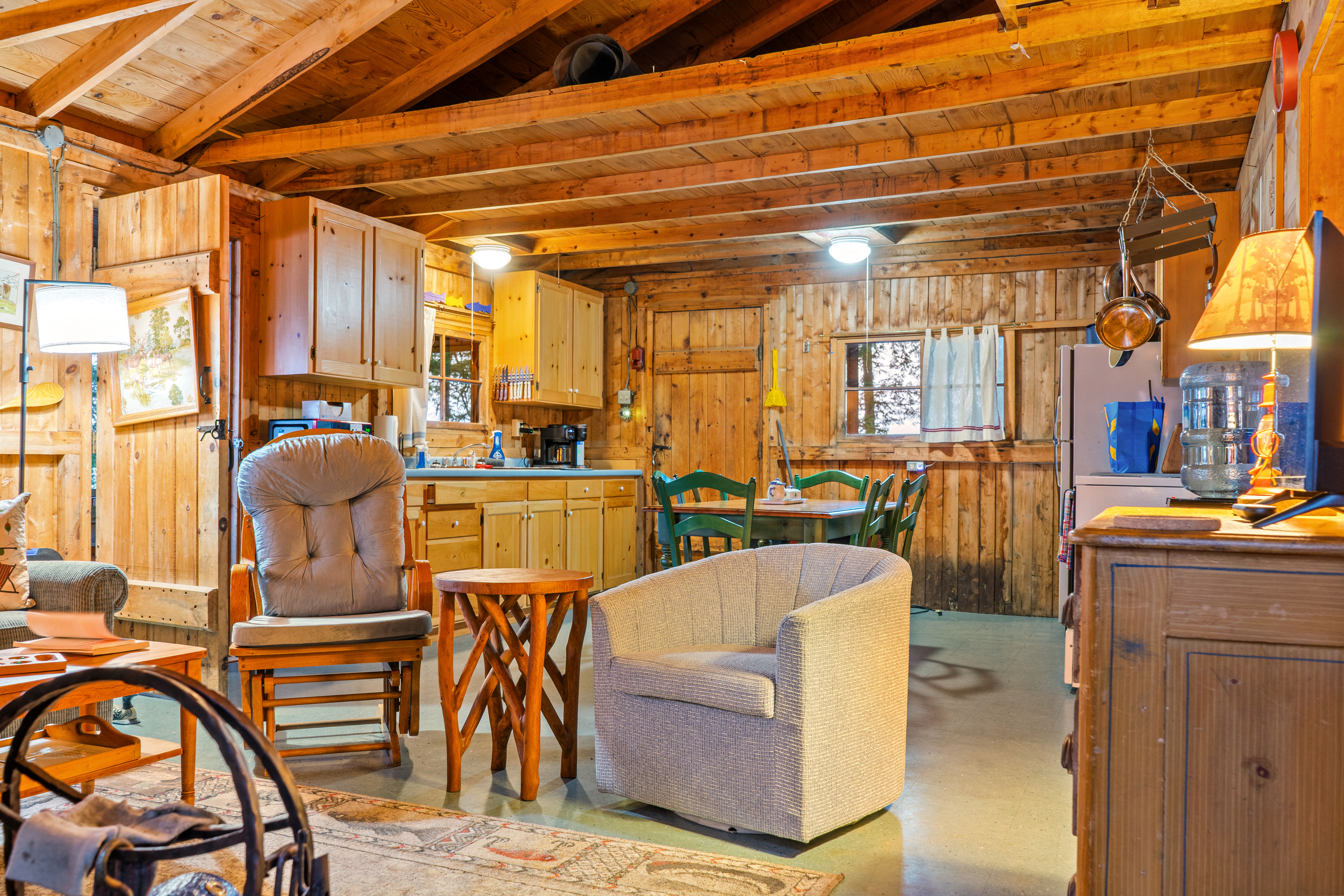 First step inside Loonrise Point! Warm knotty pine interior, exposed rafter ceilings, and cozy seating welcome you in. Open layout flows seamlessly into the fully equipped kitchen and dining area on Beech Hill Pond in Otis, ME. Timeless camp charm!