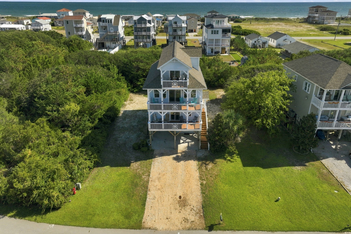 Aerial view of the home surrounded by lush coastal greenery, featuring a spacious driveway and multiple outdoor decks