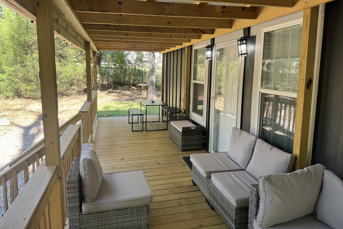 Large covered porch with sectional sofa, coffee table, and dining set, perfect for relaxing in the woods
