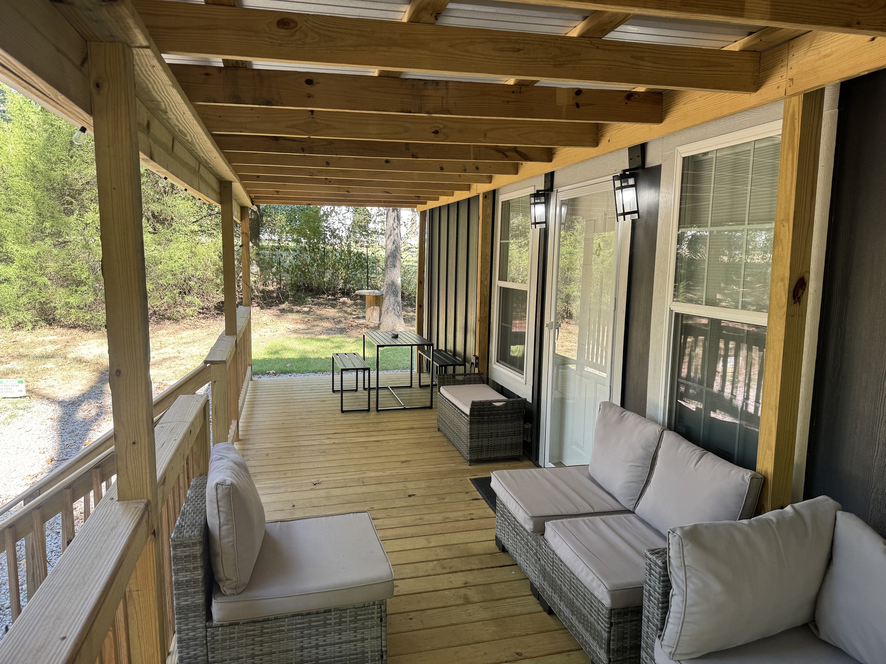 Large covered porch with sectional sofa, coffee table, and dining set, perfect for relaxing in the woods