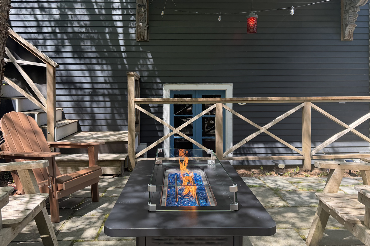 Blue glass flames dancing on the stone quarterdeck. This shot looks past the fire table to the red port navigation light, marking the direct entryway down into the ship's wood-planked "Below Deck" mess hall for evening gatherings.