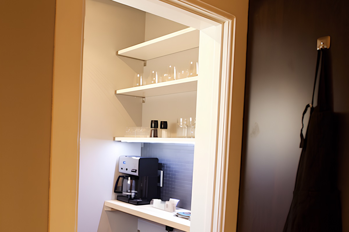 Pantry next to kitchen holds coffee pot, mugs and glassware