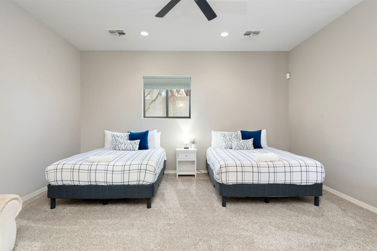 Spacious casita bedroom with two queen beds, ceiling fan, and soft neutral tones—perfect for families or groups needing extra sleeping space.