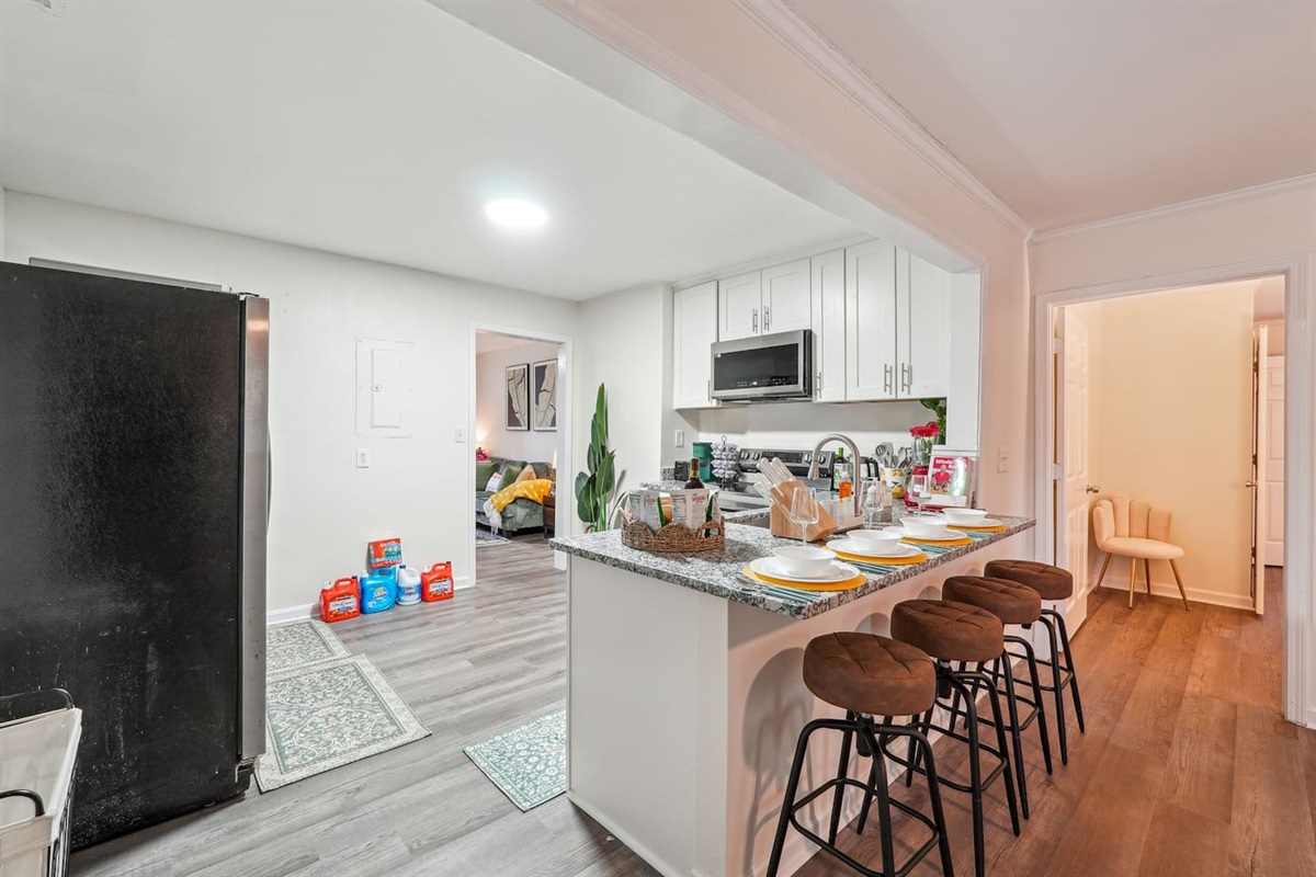 A fully equipped kitchen with a refrigerator, microwave, stove, oven,fridge, dishwasher, coffee maker, kettle, toaster, and blender. Includes plates, bowls, utensils, pots, and pans, plus four bar chairs for casual dining or socializing.
