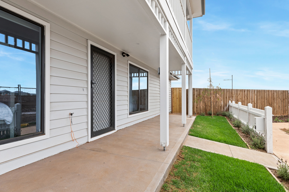 Covered ground-floor verandah with a paved floor and security screen door, beside a small lawn and the picket fence.