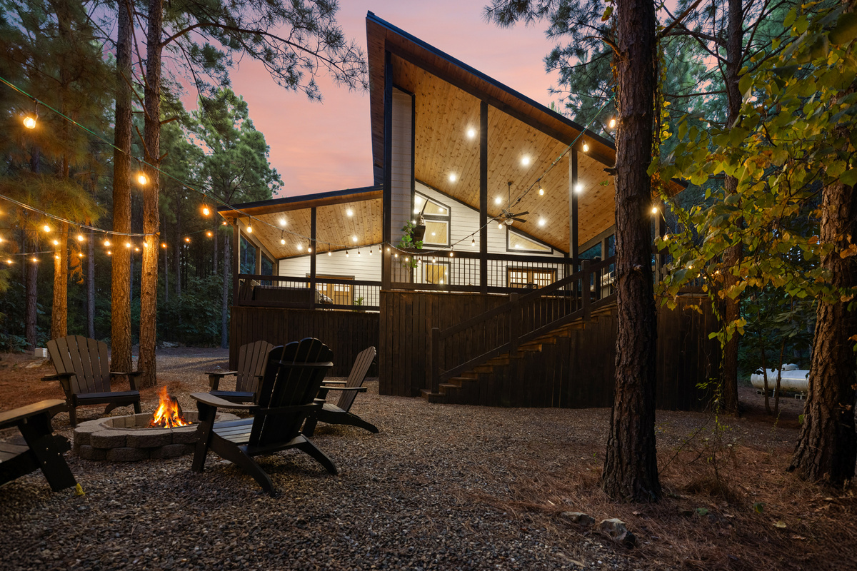 This is Cedar Stillness after dark: the cabin glowing beneath the pines, string lights overhead, and the fire pit ready for one more round of stories.