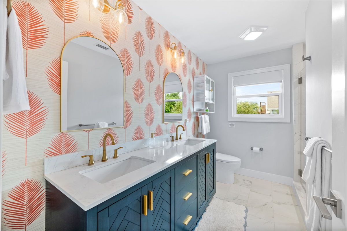 A touch of tropical elegance! The master bathroom features a double vanity and charming coral palm wallpaper, adding a pop of color to the sleek white marble and creating a relaxing, stylish retreat.