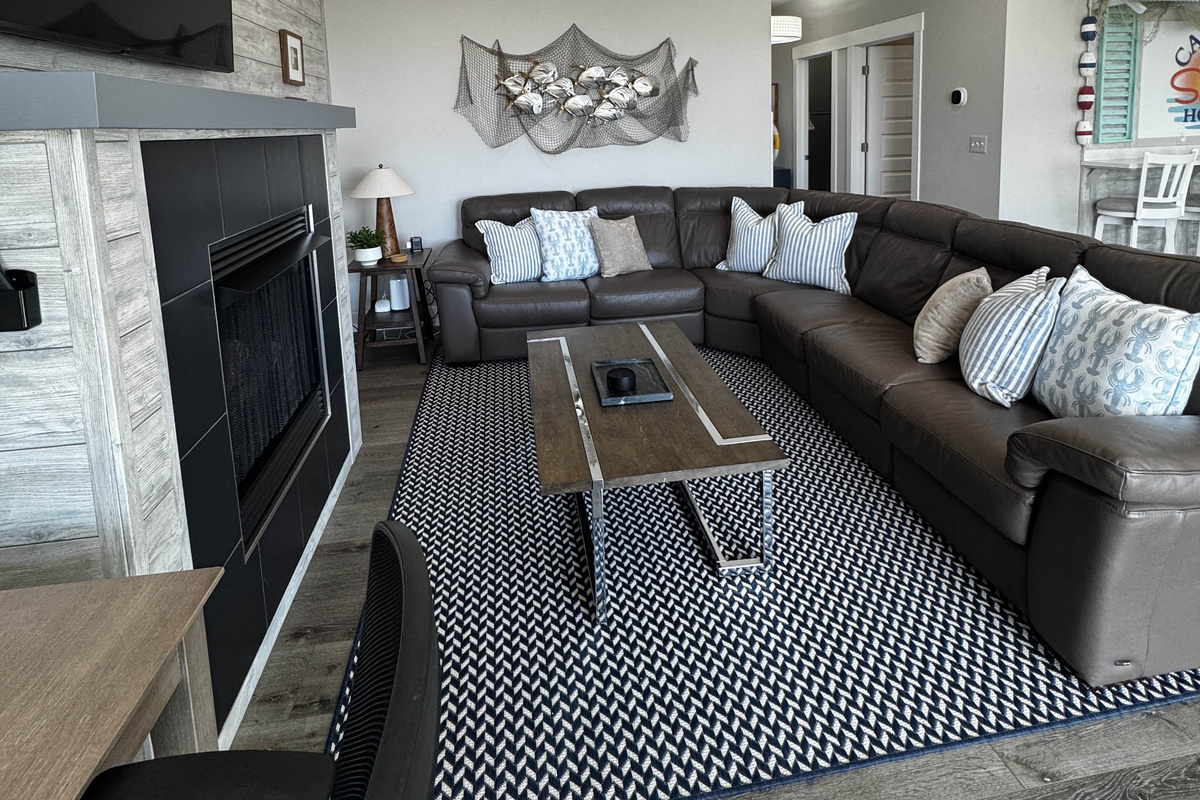 Cozy living room with a large sectional sofa, modern fireplace, and coffee table, set on a stylish patterned rug—perfect for relaxing and gathering with family or friends.