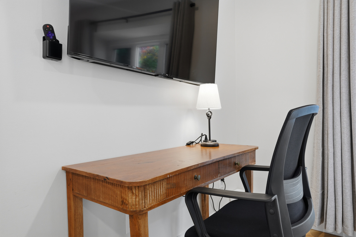 Comfortable workspace featuring a wood desk, ergonomic chair, and wall-mounted TV. A clean, quiet setup ideal for remote work, studying, or catching up on emails during your stay.