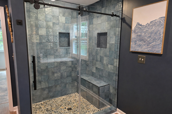 Walk-in tile shower in the main-floor primary bath with glass doors, bench seating and a clean spa-style feel.
