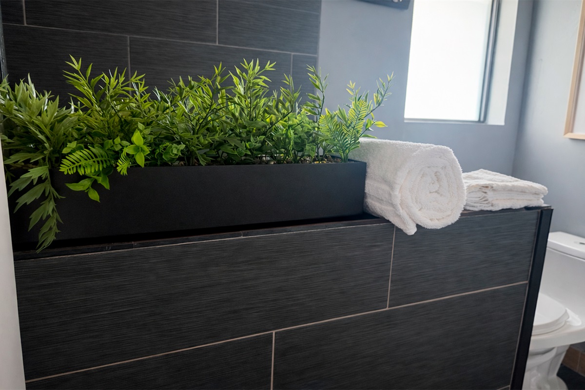 Thoughtful bathroom details in The Red Room, with fresh greenery, soft white towels, and modern dark tile finishes.
