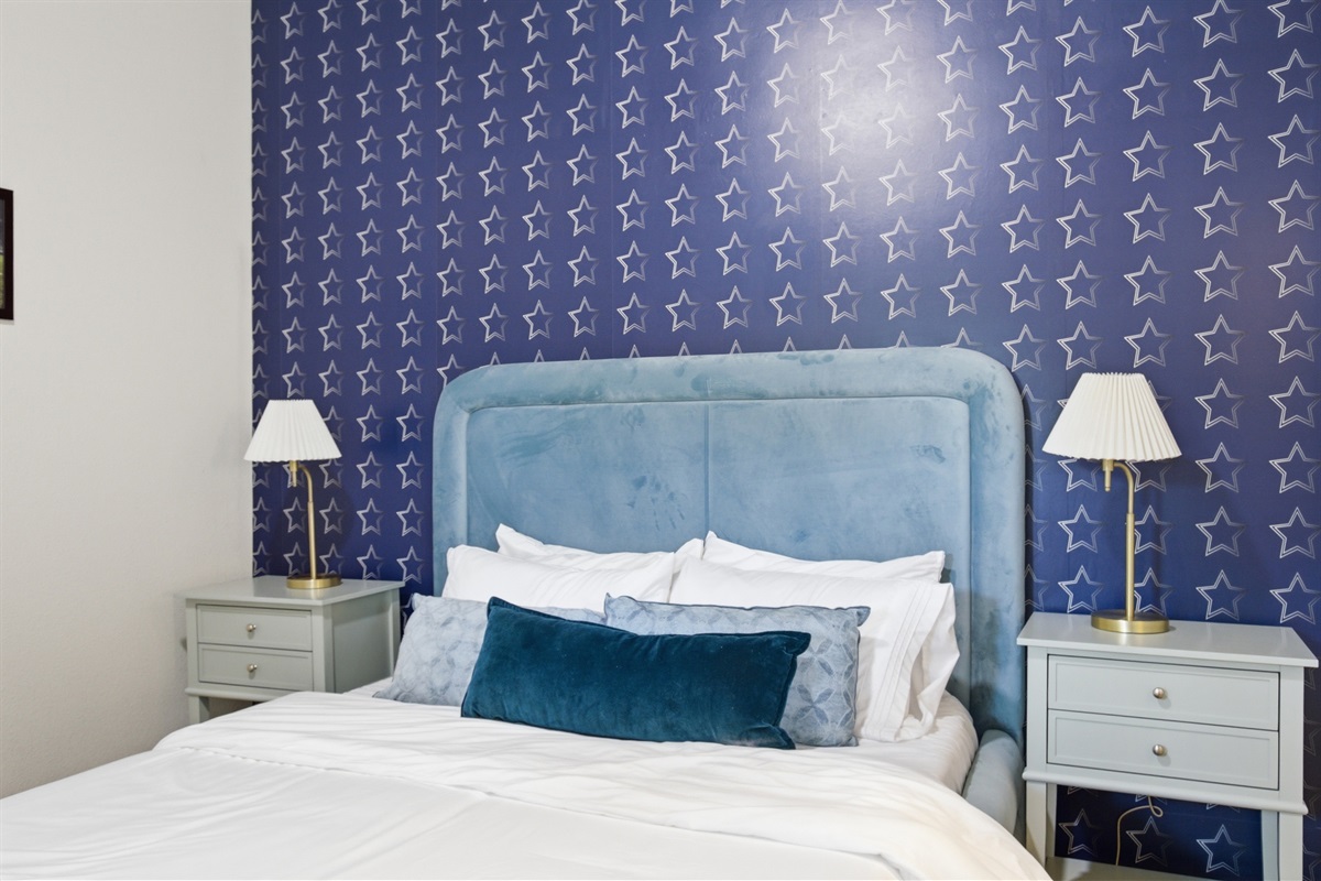 Double bed close-up with blue headboard and crisp white bedding. Extra pillows, blankets, and room-darkening shades provided. One of four private bedrooms.
