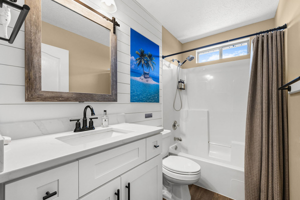 Bright and beautifully styled guest bathroom. Featuring a modern white vanity with matte black hardware, a custom shiplap accent wall, a rustic wood-framed mirror, and a handy hair dryer for your convenience. The full shower/tub combo includes an adjustabl