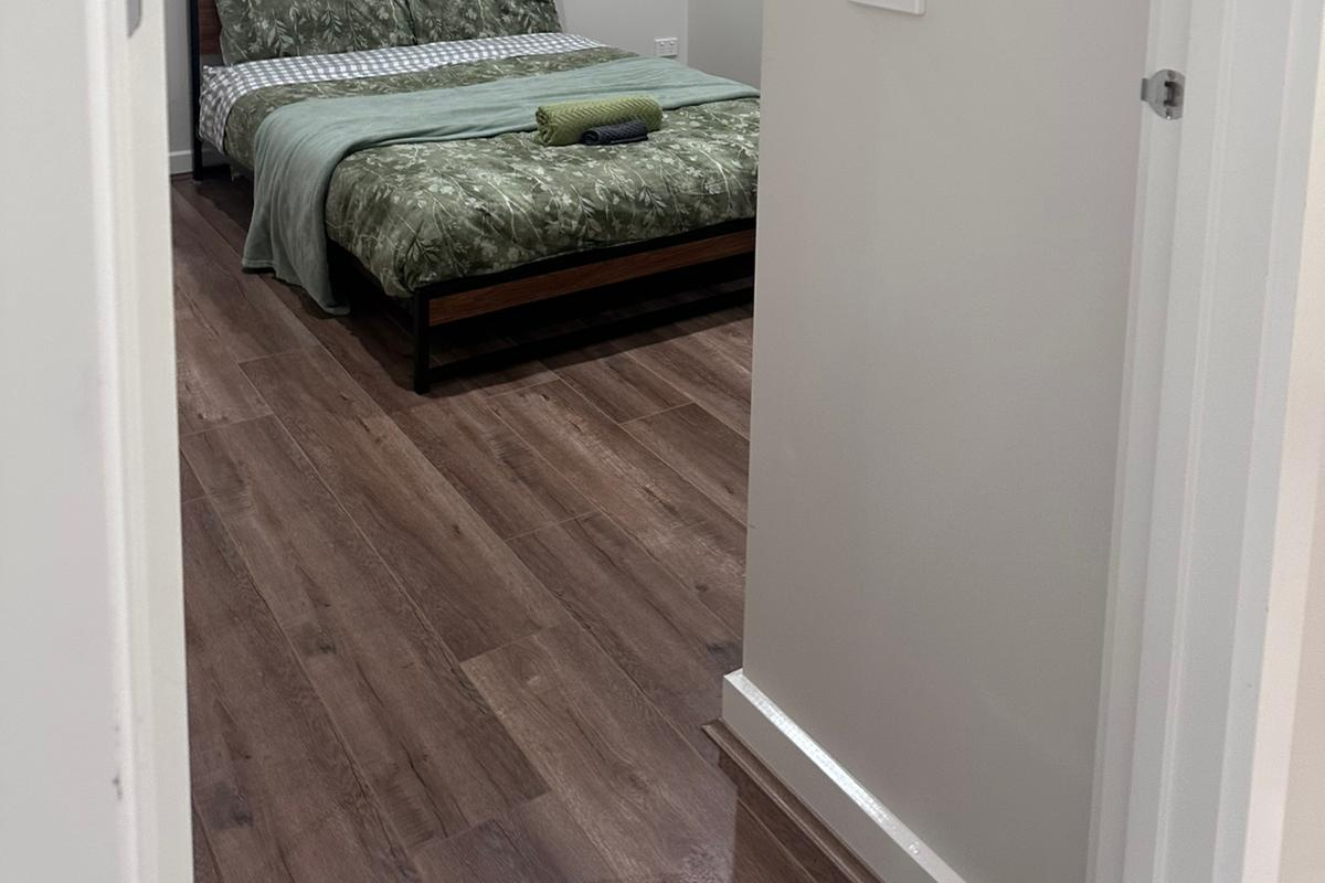 The bedroom includes a comfortable bed, leafy green bedding and open floor space, creating a practical sleeping room within the home.