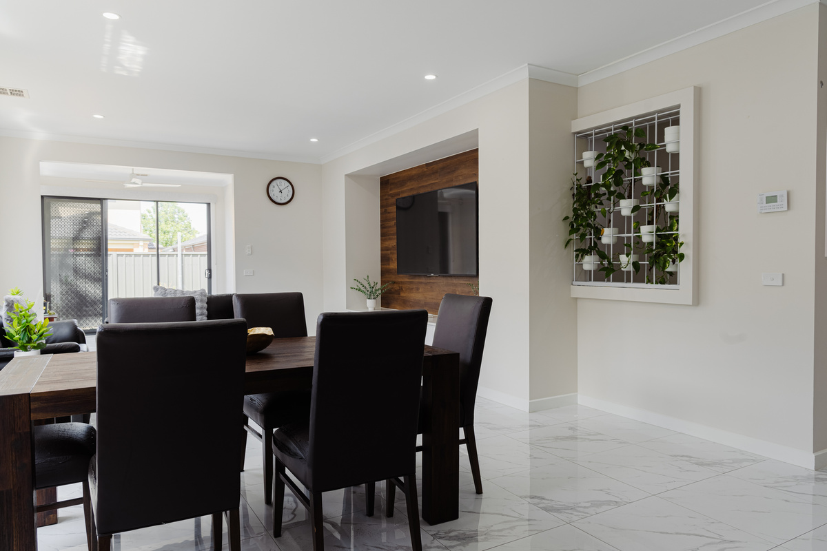 Open-plan dining and living area with dining table, lounge seating and wall-mounted TV.
