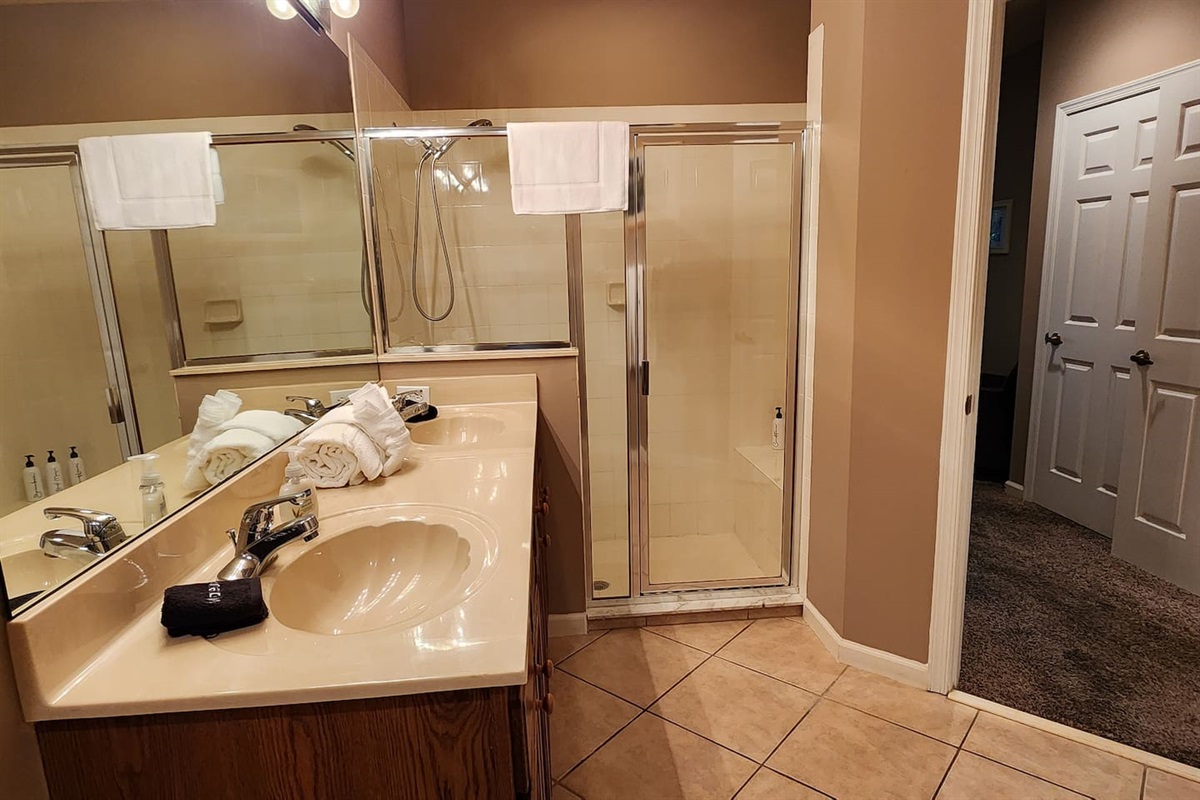 Bright bathroom with a large vanity, walk-in shower with glass doors, and tile flooring.