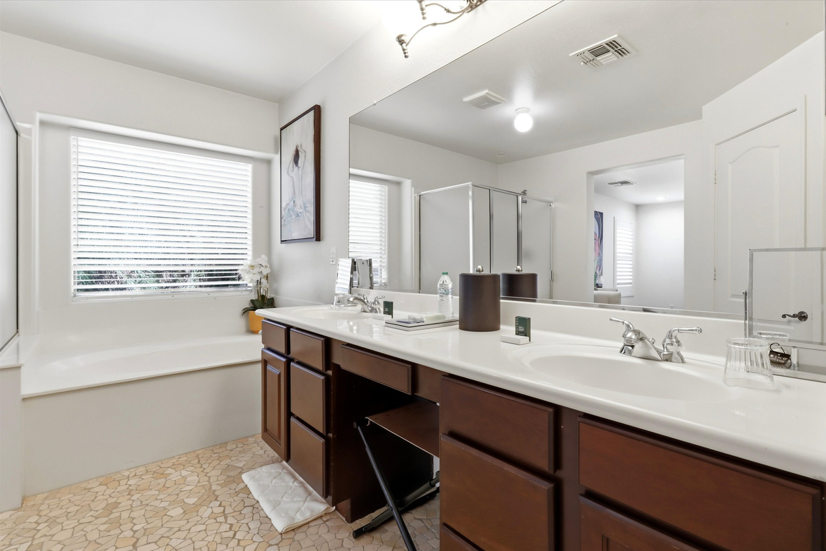 Bathroom vanity with double sinks, a makeup chair, storage drawers, and a soaking tub nearby.
