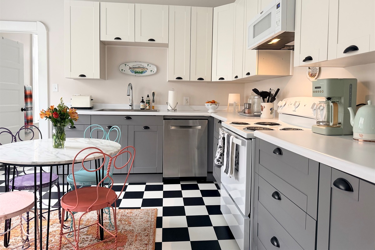 A bight, timeless full kitchen featuring classic black-and-white checkered floors, marble top bistro table for four, and generous prep space  - playful, practical and designed for real stays.