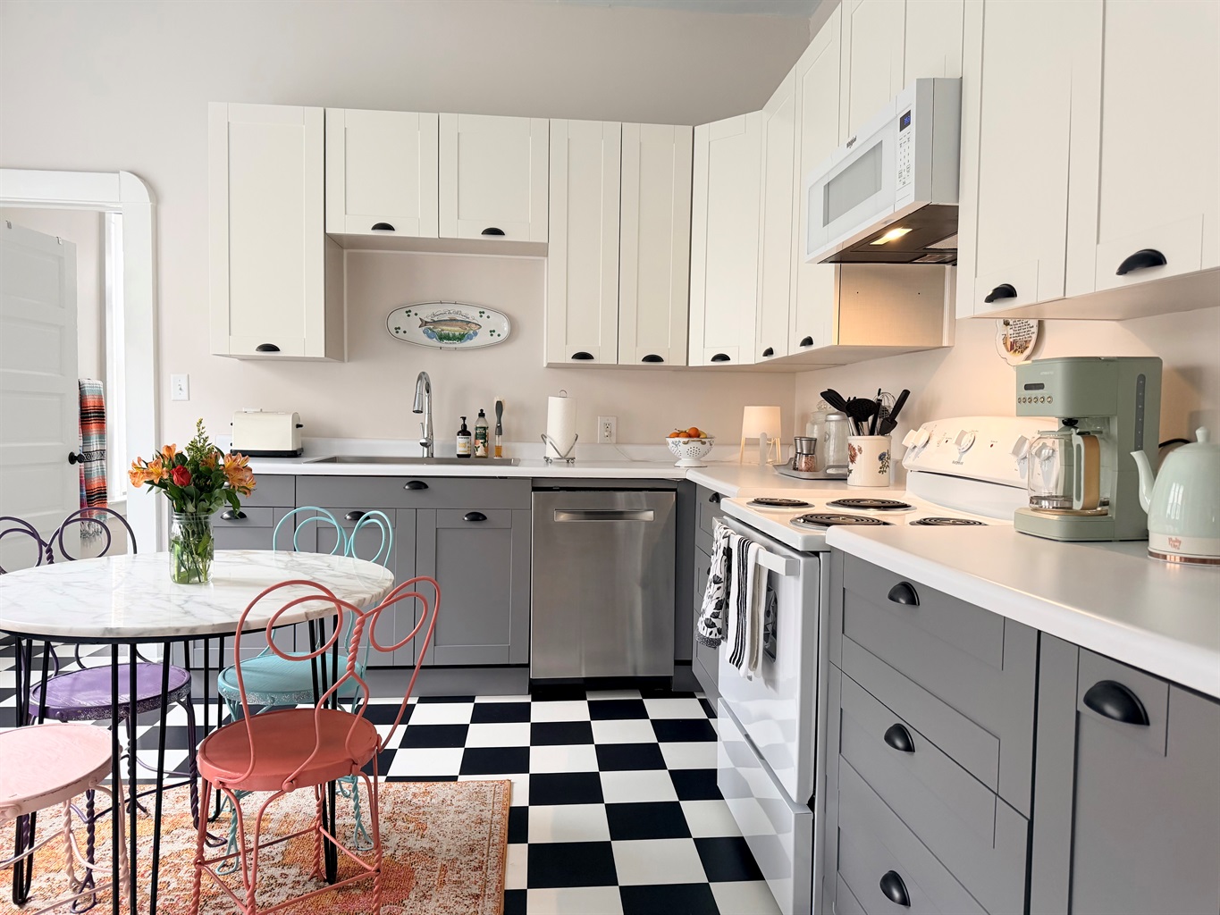 A bight, timeless full kitchen featuring classic black-and-white checkered floors, marble top bistro table for four, and generous prep space  - playful, practical and designed for real stays.