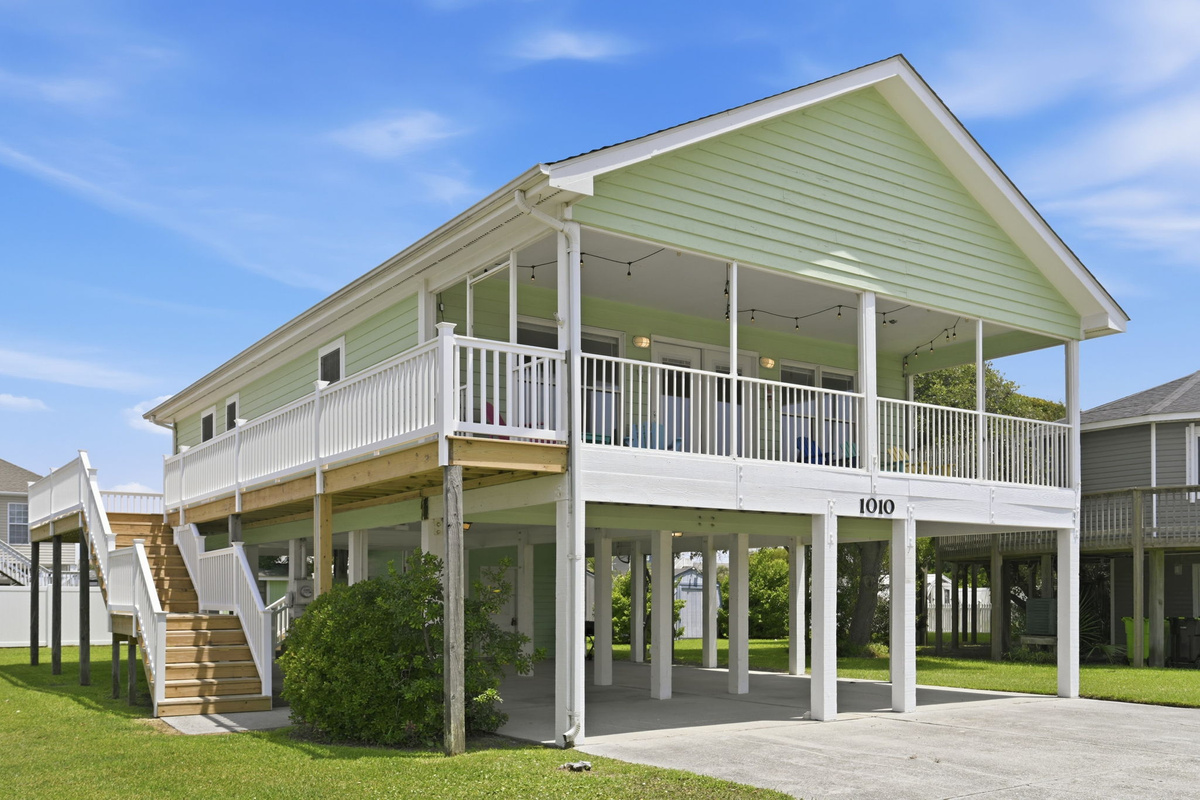 Bright coastal home featuring a large wraparound screened porch, covered parking, and plenty of outdoor space