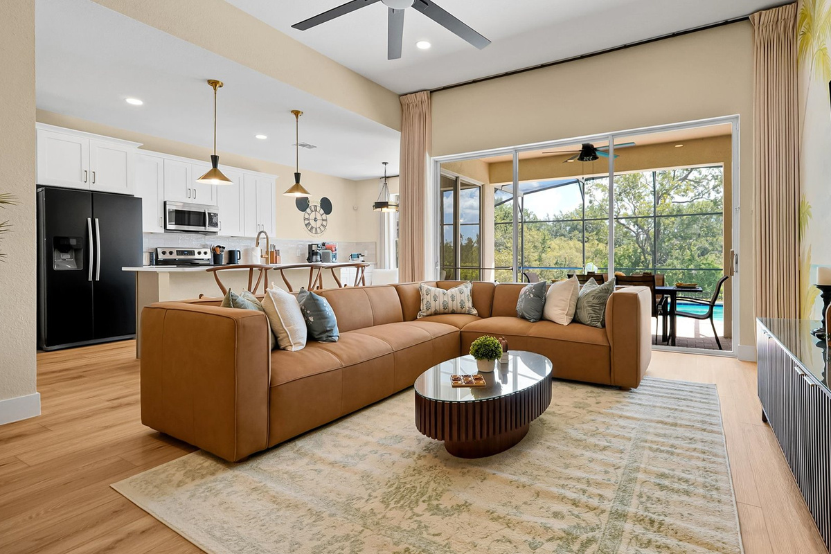 Living Room: Spacious open-concept living room with a large sectional, TV and direct access to the covered poolside lanai.