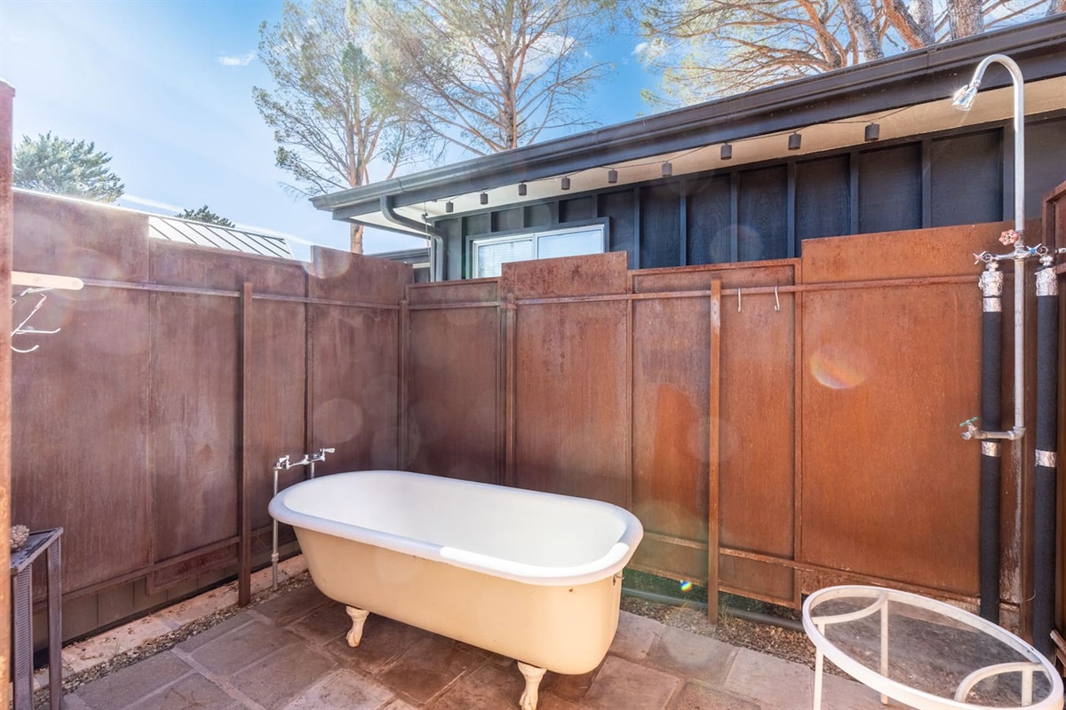 Private outdoor soaking tub with open-air shower, enclosed by rustic wood fencing for a serene spa-like escape.