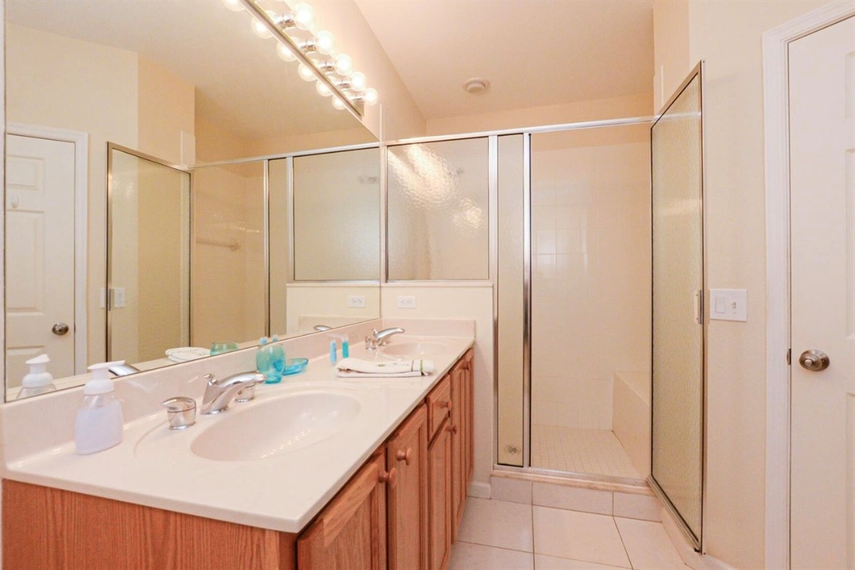 Bright bathroom featuring a large vanity, full mirror, tile flooring, and a walk-in shower with glass doors.