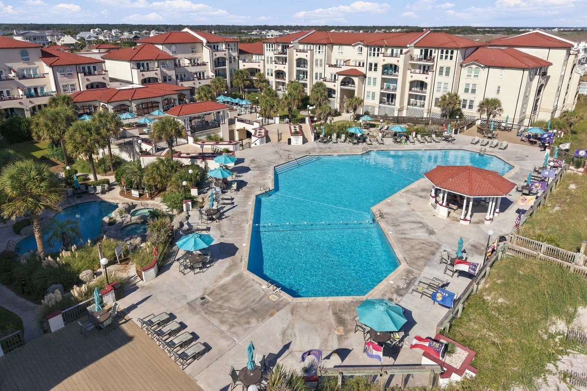 Pool patio deck with a central swimming basin, poolside gazebo, lounge chairs, shade umbrellas, and palm landscaping bordering the residence buildings.