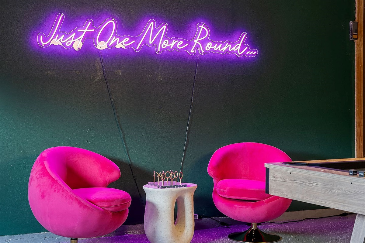 Immerse yourself in a playful atmosphere with vibrant pink chairs and a neon sign, perfect for casual conversations and fun.