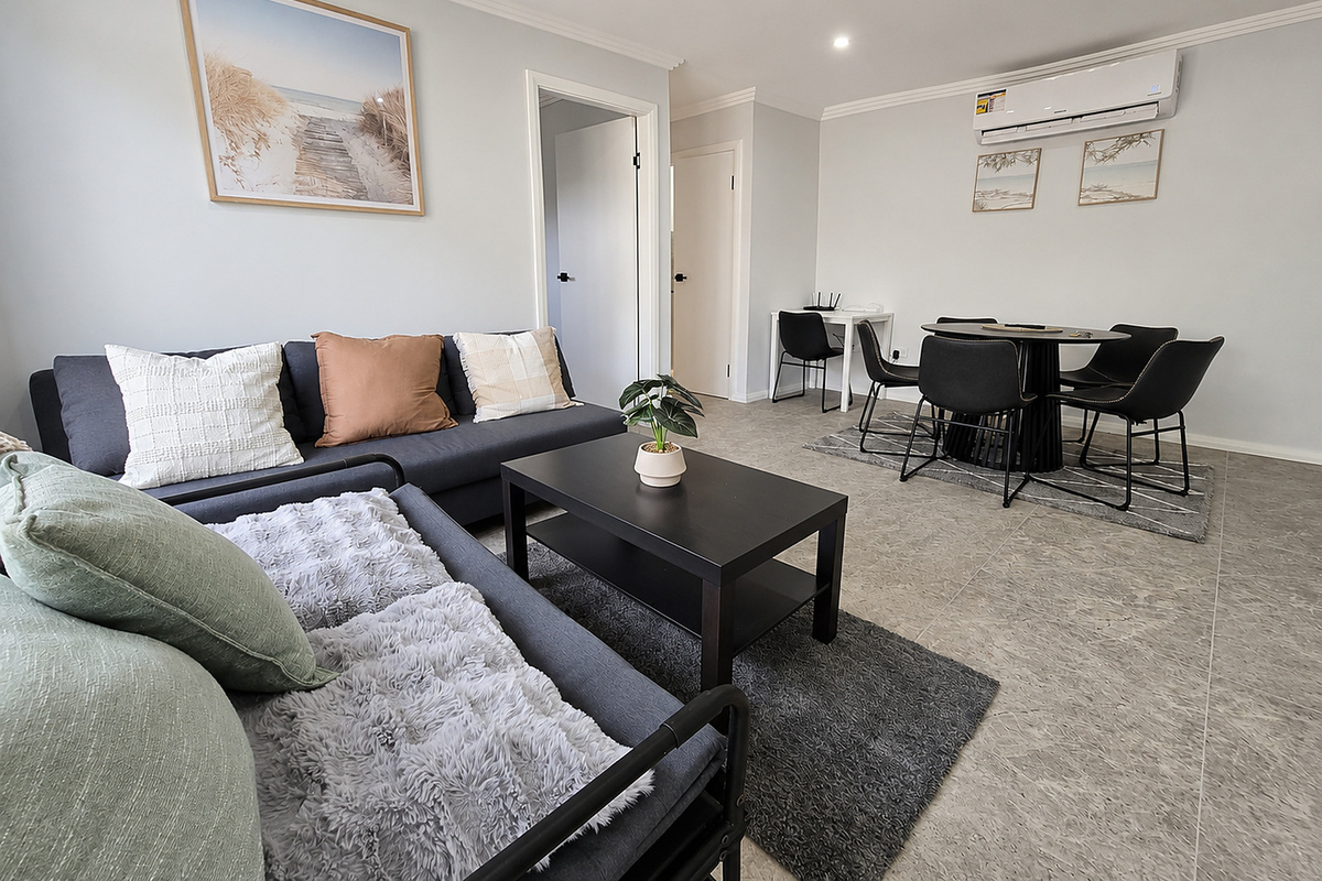 Matilda’s Urban Escape opens into a combined living and dining area with lounge seating, a round dining table and light grey tiled flooring.