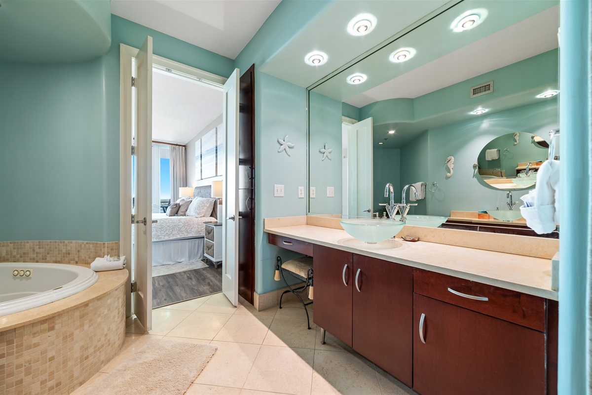 Discover the exquisite details of the primary bathroom: a beautifully tiled soaking tub, a modern vanity with a unique glass sink, and direct access to the tranquil bedroom. Experience comfort and sophistication.