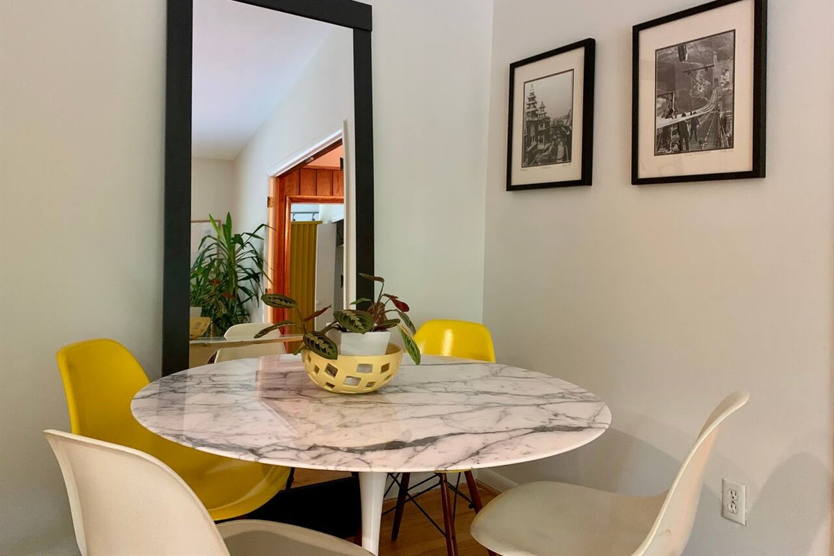 The breakfast nook, off the kitchen, features a buttery leather couch and this marble dining table with seating for 4. Playful Eames chairs pick up and continue a fun theme of yellow highlights throughout the house. Walls: San Francisco photography.