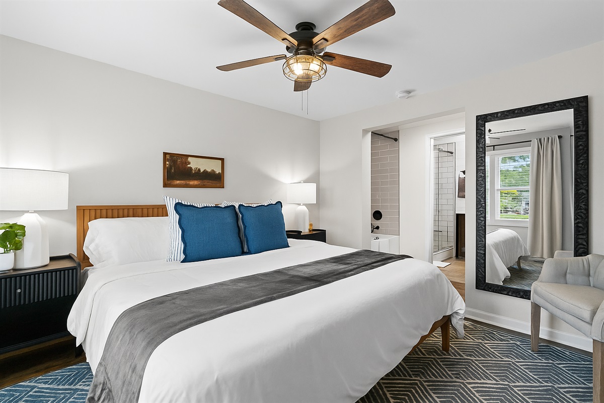 Elegant king bedroom with full-length mirror, ceiling fan, and cozy touches for a restful night’s sleep.