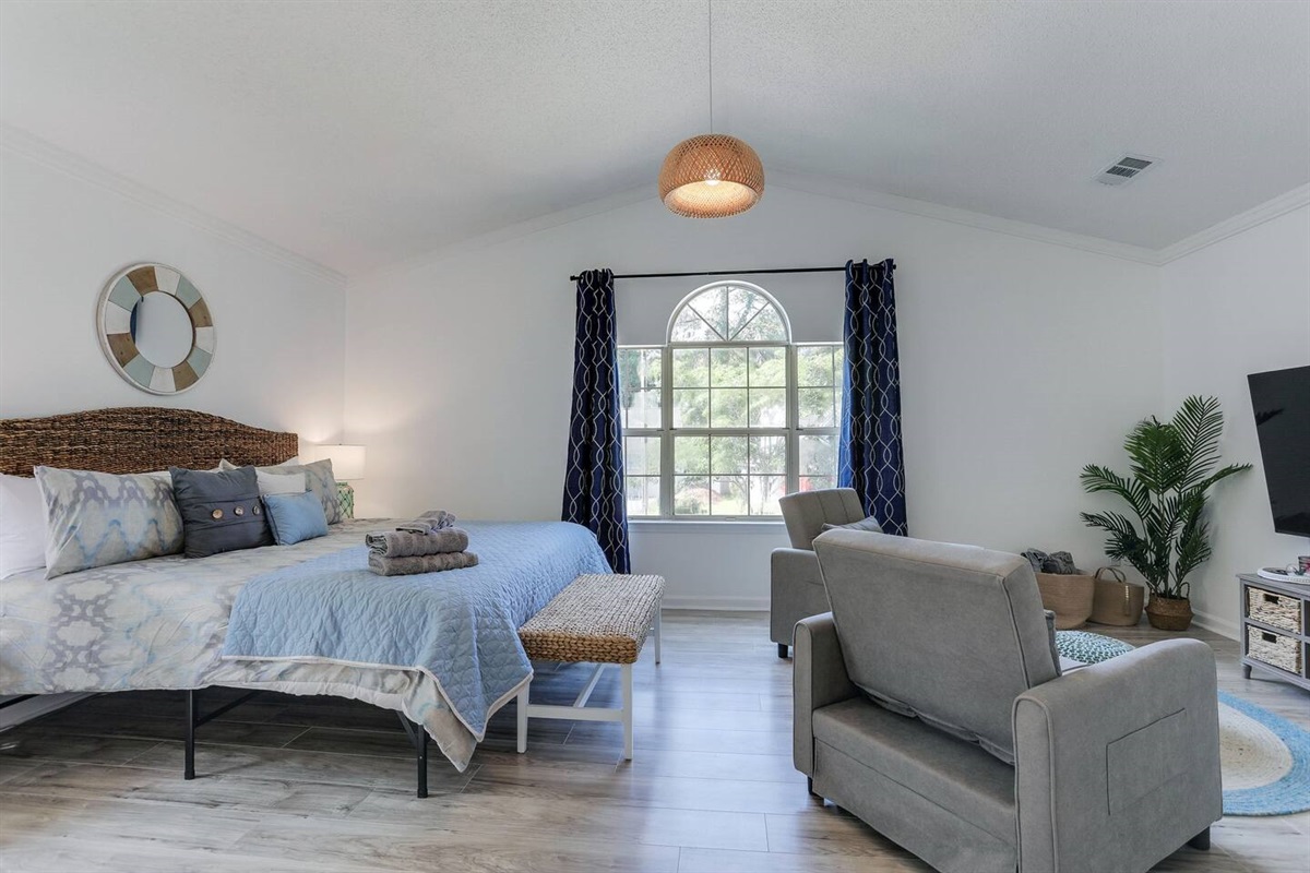 The primary bedroom at is a relaxing retreat, complete with a luxurious king-sized bed, a smart TV for your entertainment, an ensuite bath for added privacy, and two cozy side chairs, perfect for unwinding after a day of exploring.