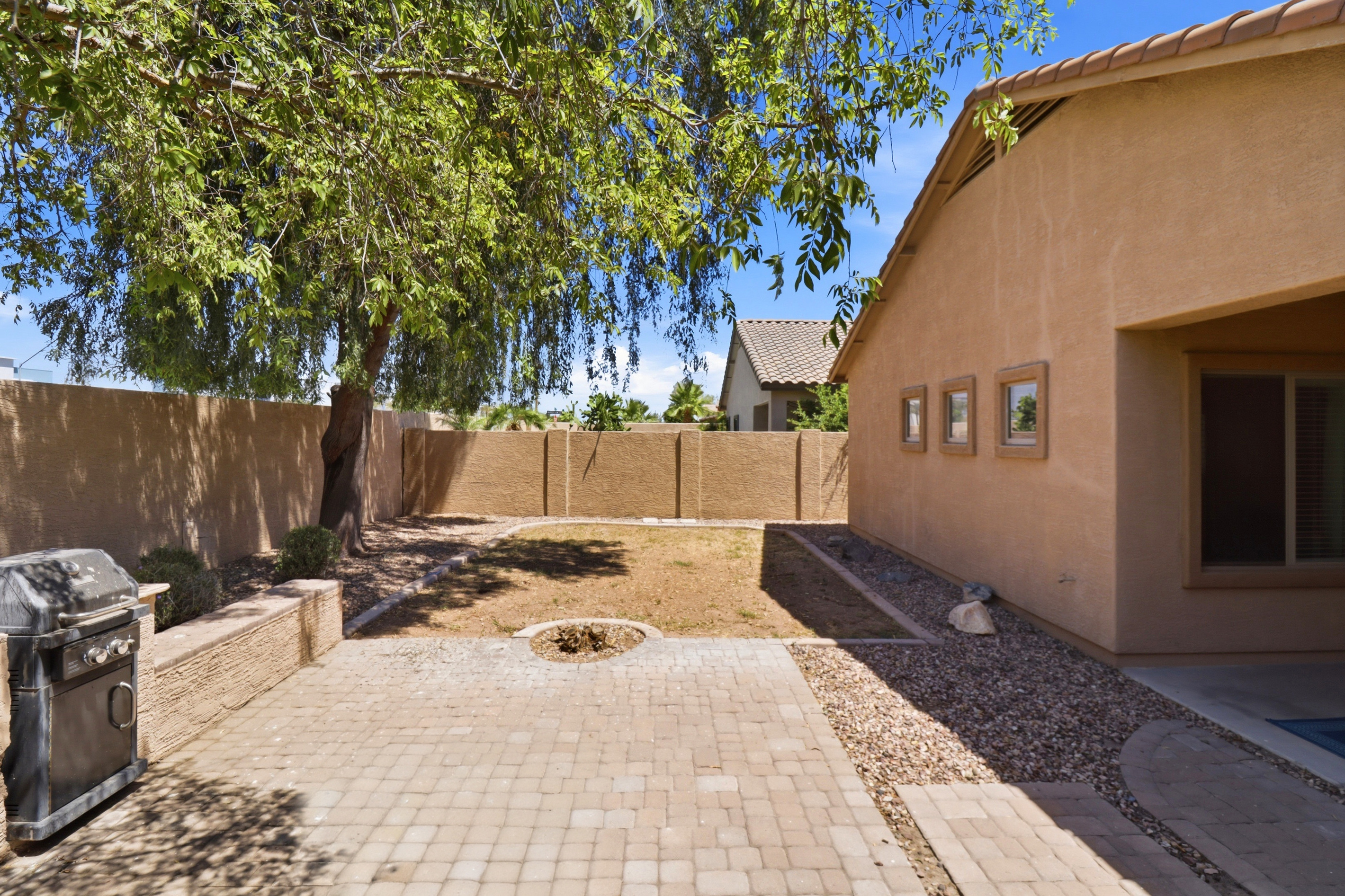 Fenced backyard with shade from the tree, a BBQ grill, and space to spend time outside.
