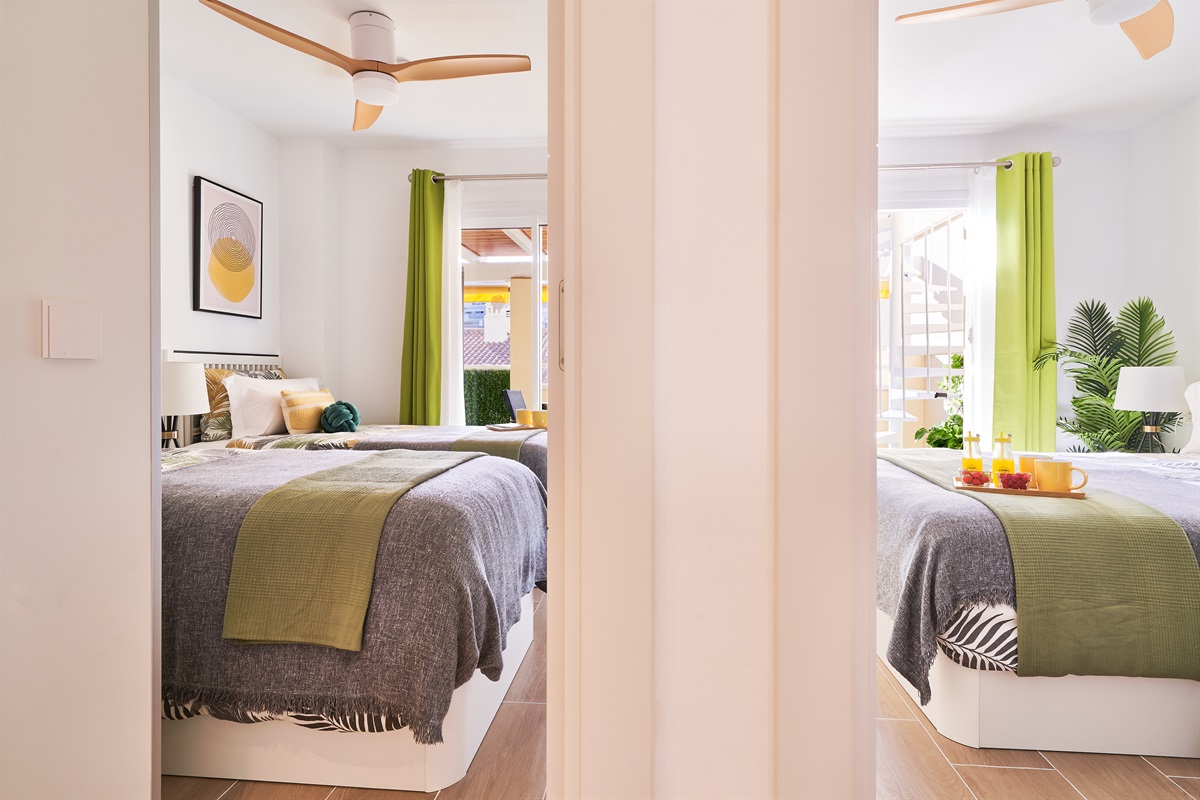 Bright and calming twin bedroom with tropical tones, soft linens, and direct access to the terrace — perfect for relaxed mornings and restful nights.