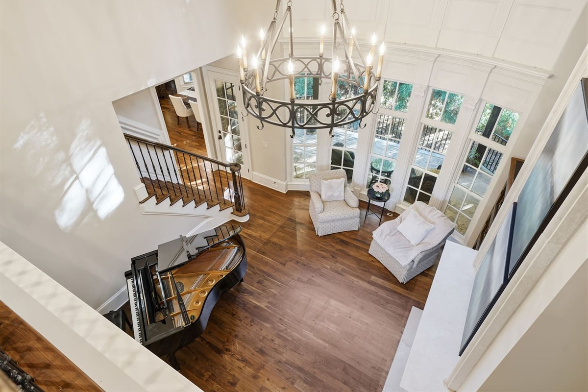Beautiful entry sitting room with a grand piano, warm fireplace, tall windows, and two comfortable chairs. A bright, serene spot to unwind or enjoy quiet moments.