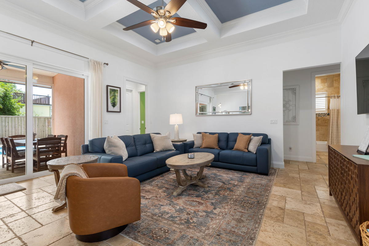 Navy sofas and a cognac swivel chair under a coffered ceiling, with sliders to the patio for easy pool-to-sofa days.