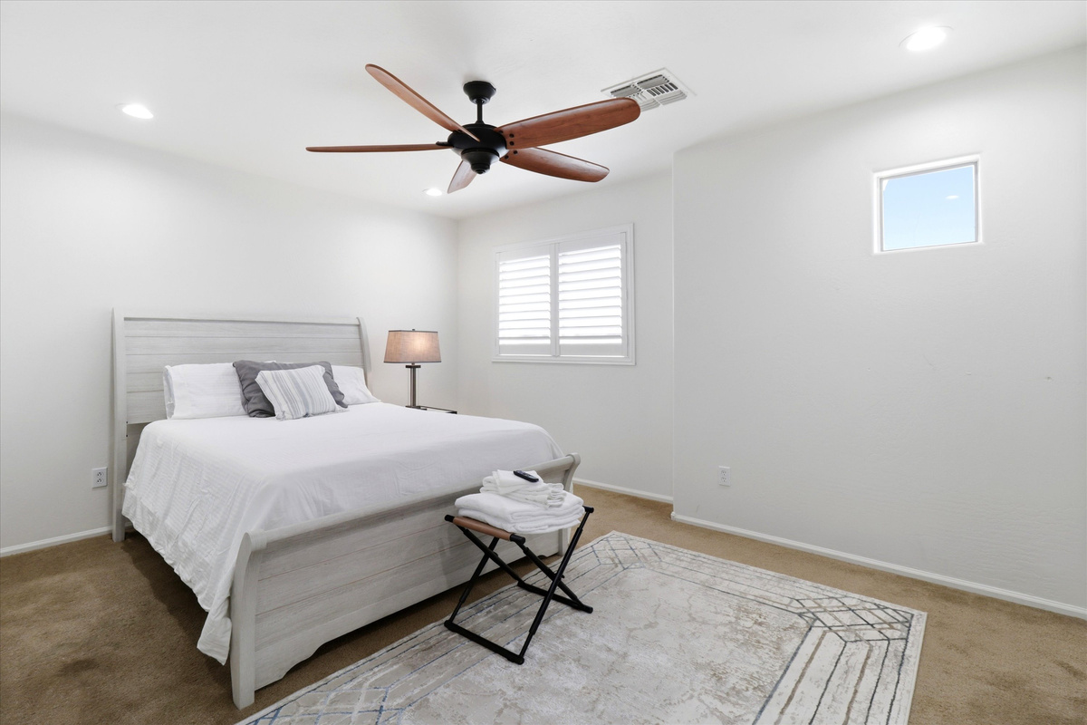 Bedroom with a clean bed setup, ceiling fan, and space to settle in.
