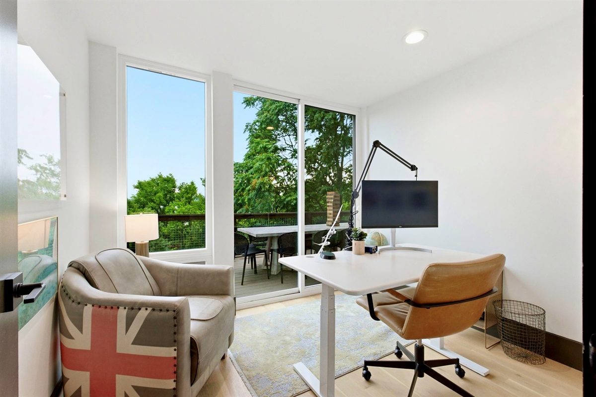 Minimalist home office w/ a wood desk, Eames-style chair & leafy garden views to spark focus.
