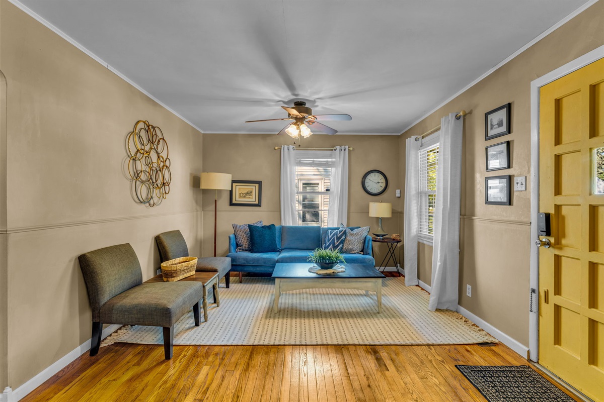 Cozy living room with comfortable seating, a ceiling fan, and two windows that can fill the room with natural light.