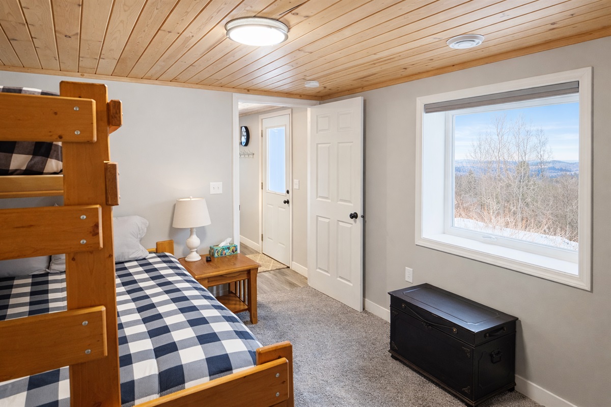 In this view of the downstairs bedroom, the window frames a peaceful glimpse of Lake Superior and the backyard. With natural light streaming in, this cozy space offers a serene connection to the outdoors while you relax or recharge.