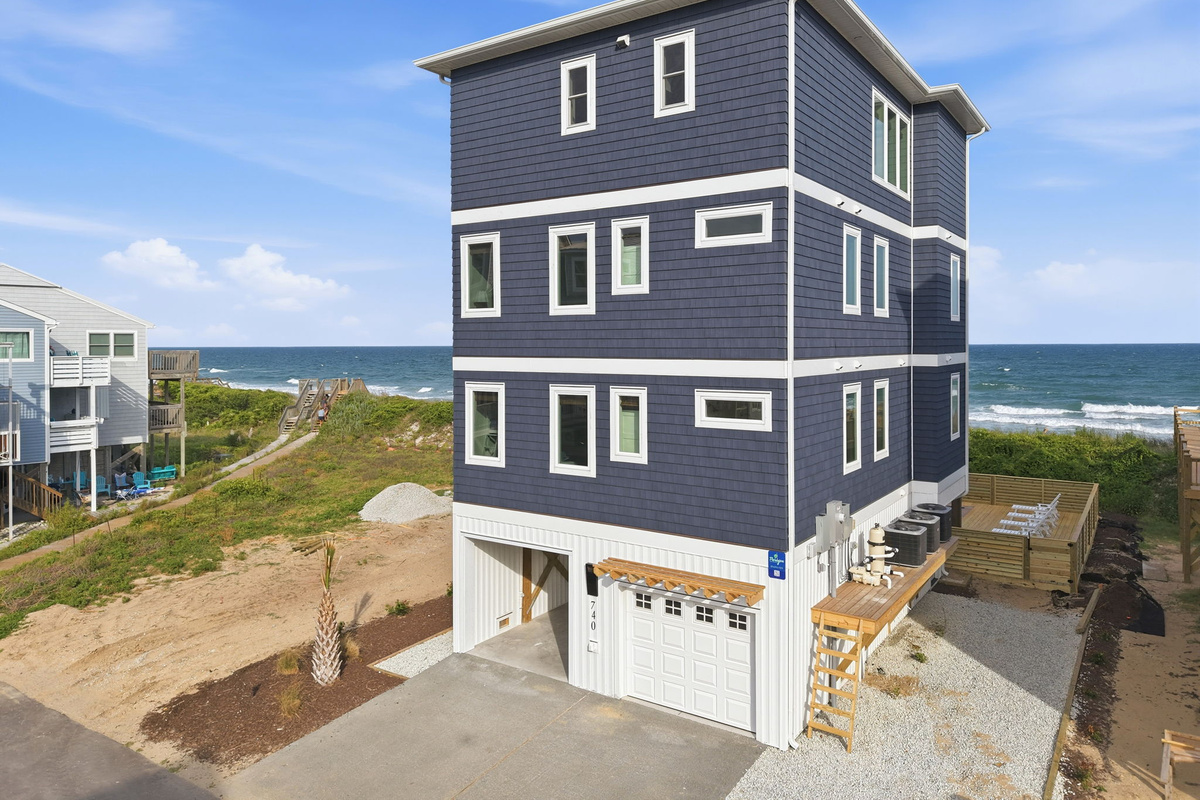 Rear/side exterior view of the property showing driveway-side elevation, outdoor utility equipment, and elevated coastal construction with ocean proximity and neighboring beach homes