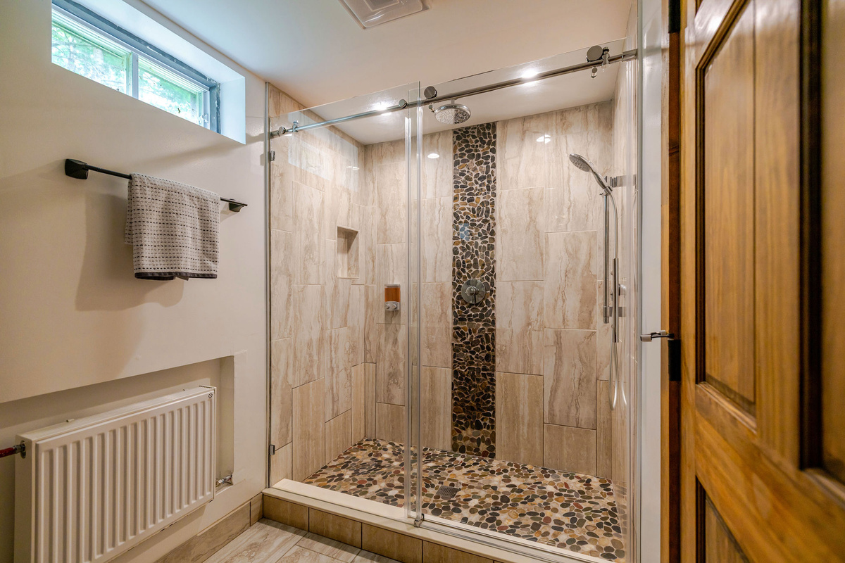 Refresh in the beautifully tiled walk-in shower, featuring a frameless glass enclosure and spa-inspired finishes in the lower-level bathroom.