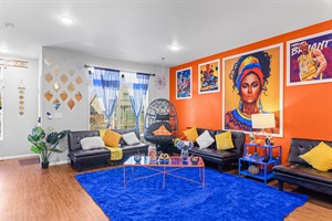 Relax in a colorful, art-filled living room that blends comfort with cultural flair, featuring striking wall art, bold orange accents, and luxurious leather couches for a truly unique experience
